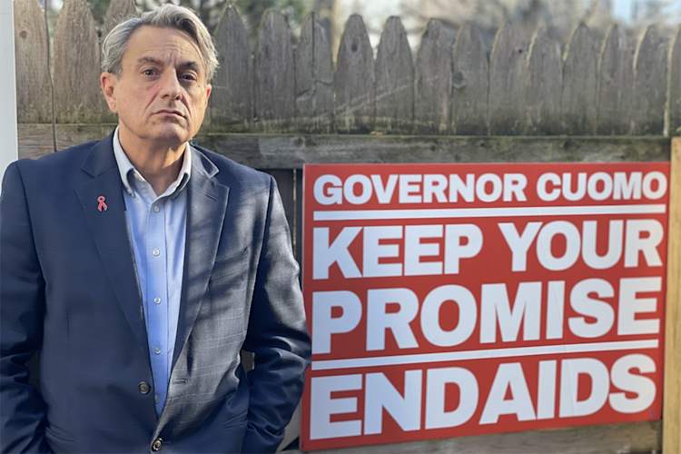 Perry Junjulas next to a sign that says "Governor Cuomo Keep Your Promise End AIDS'
