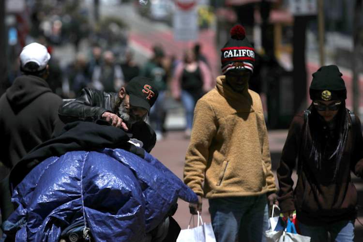 Pedestrians walk by a homeless man as he arranges his belongings on a cart on May 17, 2019 in San Francisco, California