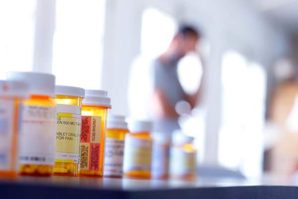 multiple prescription pill bottles with man in the background