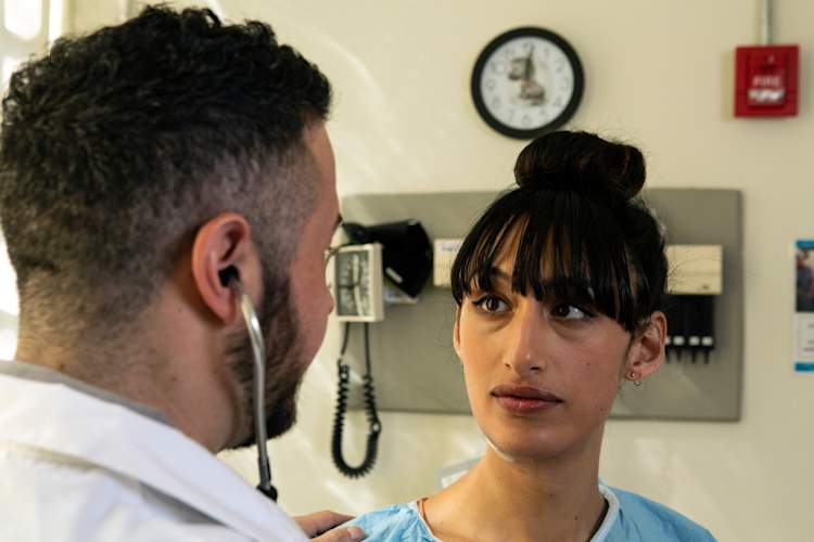A transgender woman in a hospital gown being treated by a doctor