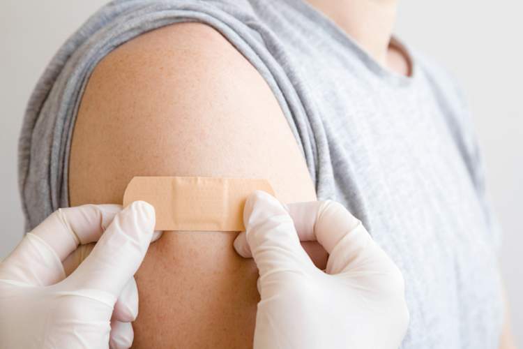 Doctor in white gloves putting bandaid on young man's arm after giving vaccine