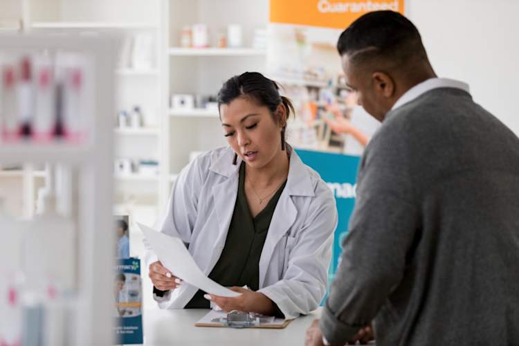 pharmacist reviews prescription with customer