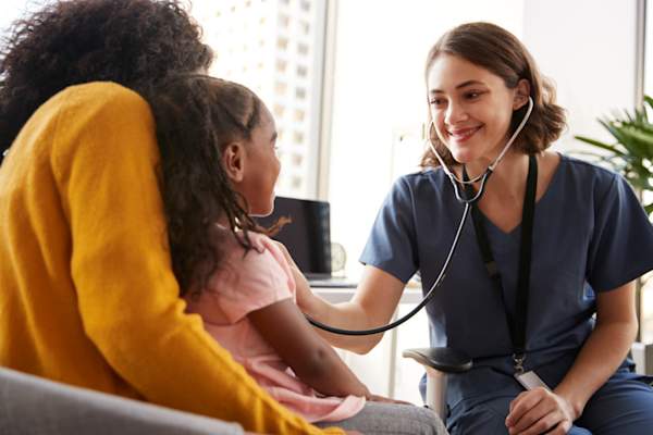 Female Pediatrician Wearing Scrubs Listening To Girls Chest With Stethoscope