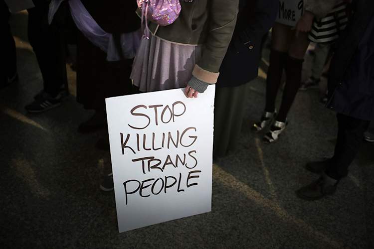 Person holding protest sign reading "Stop killing trans people"