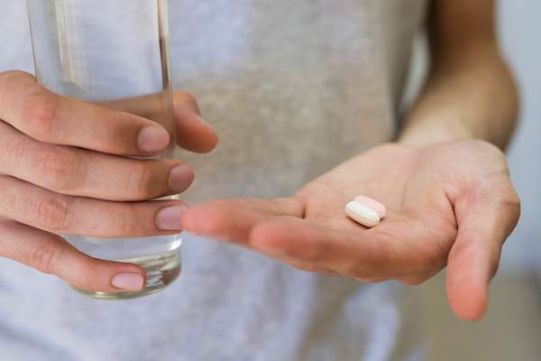 Hands with two pills and a glass of water