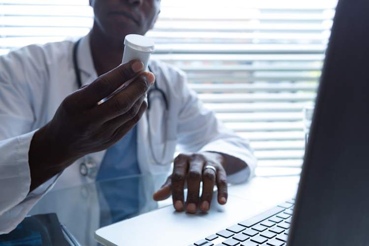 doctor with pill bottle and laptop