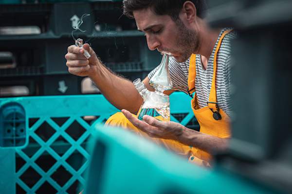 man in yellow overalls smoking cannabis out of glass bong