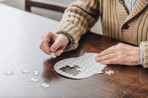 Cropped view of senior man playing with puzzle shaped like head