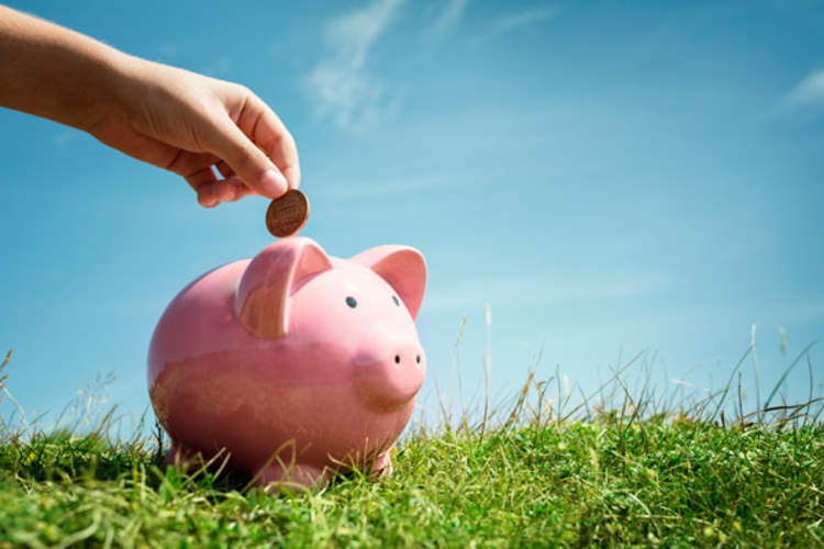 A hand placing money in a piggy bank