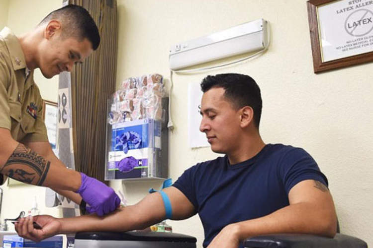 Navy Petty Officer 1st Class Oliver Arceo draws blood from a sailor for routine HIV testing