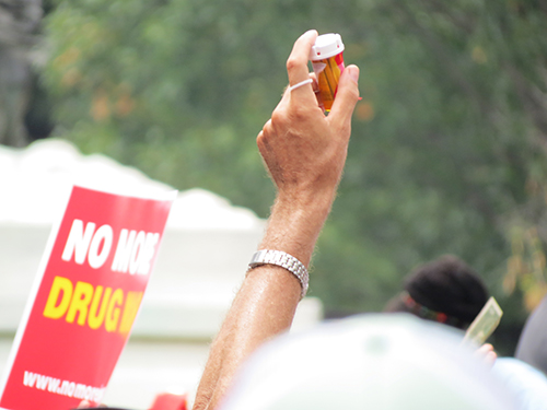 A protestor holds aloft a symbolic pill bottle stuffed with dollar bills that would be tied to the White House gate.
