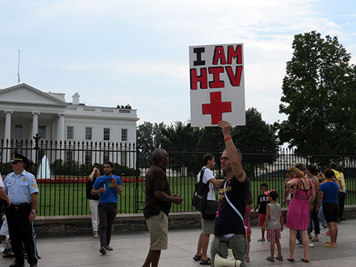 A protestor mingles with tourists on the sidewalk in front of the White House.