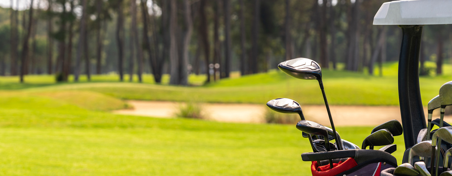 Primo piano di mazze da golf trasportate all'interno di una golf car. Sullo sfondo, un campo da golf.