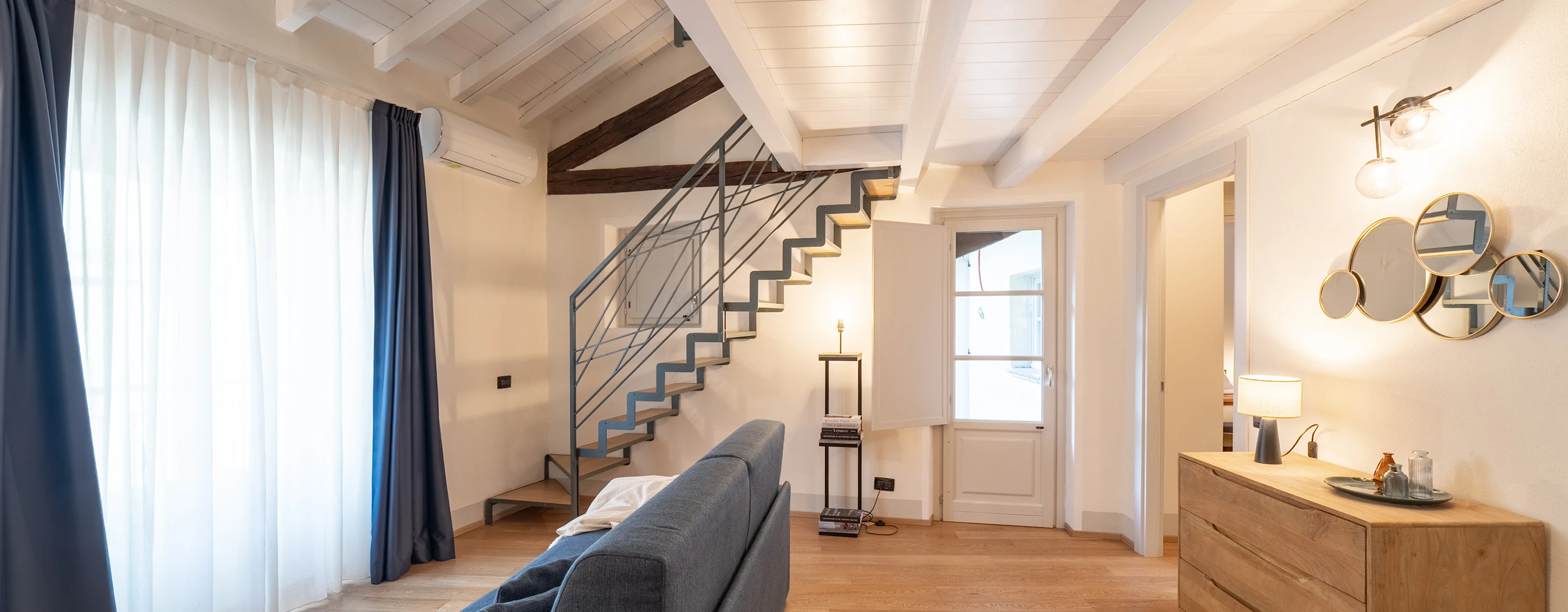 Porzione del salone con divano, madia e decorazioni alle pareti di uno degli appartamenti all'interno di Palazzo Odescalchi a Como, gestito da Wonderful Italy.