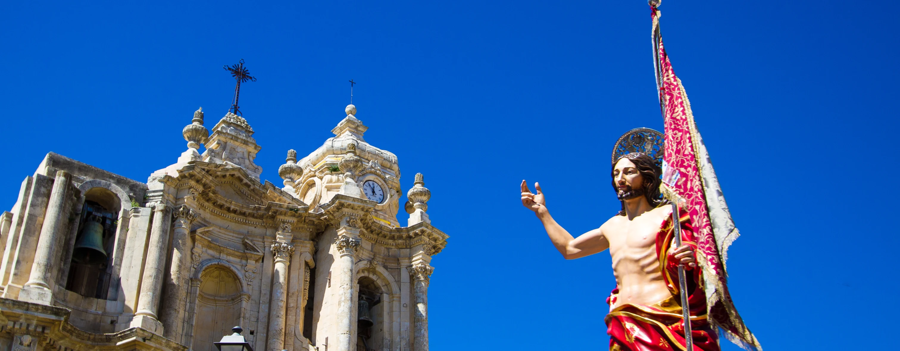 The celebration of Easter with a statue of Christ in the foreground and the Cathedral of Syracuse in the background