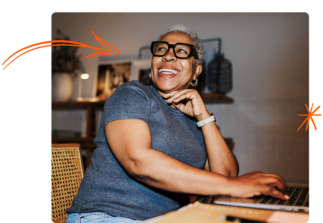 Una mujer sonriente de cabello canoso corto y gafas negras modernas trabaja en su portátil. La imagen incluye elementos decorativos naranjas: una flecha curva que apunta hacia ella y un icono de destello a la derecha.