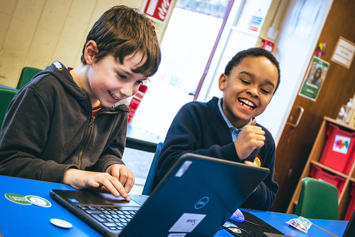 Two young Code Club members smile as they code together on a laptop