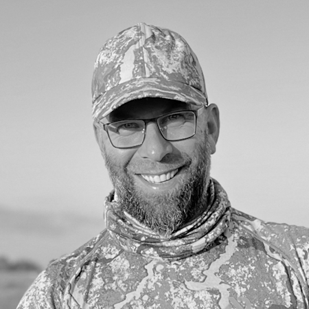 Smiling man with full beard, glasses, camouflage cap and camo neck gaiter