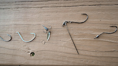 Five fishing hooks and rigs on a weathered wooden plank