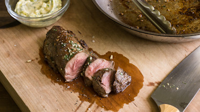 Sliced venison tenderloin with garlic herb butter, pan and knife on wooden cutting board