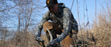 Hunter kneeling in dry grass holding a shed deer antler