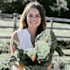 Smiling woman holding large leafy greens in a farm field with wooden fence