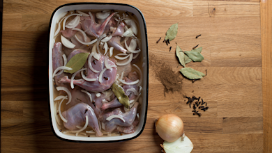 Skinned rabbit pieces marinating with sliced onion, bay leaves and cloves in a rectangular dish