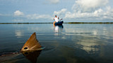 Redfish tail breaking the water, angler casting from a blue kayak under cloudy sky
