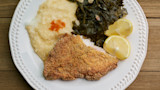 Fried catfish with grits, collard greens, and lemon slices on white plate