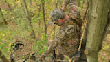 Hunter in camo cap and harness adjusting a compound bow from a tree stand