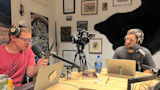 Two men wearing headphones recording a podcast at a table with camera and laptops