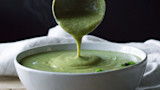 Green curry broccoli soup poured from a ladle into a white bowl