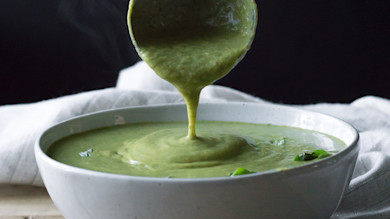 Green curry broccoli soup poured from a ladle into a white bowl