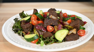 Plated elk salad with seared elk chunks, cherry tomatoes, cucumber slices, red onion, greens