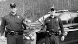 Two natural resources police hold large buck by antlers in front of truck labeled POLICE
