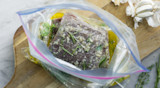 Venison steak marinating in a zip-top bag with garlic, rosemary and olive oil on cutting board