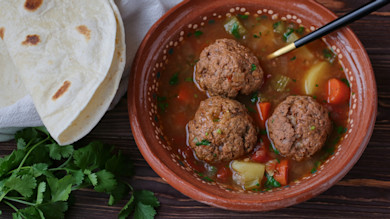 Bowl of venison meatball soup with three meatballs, carrots and potatoes, served with tortillas and cilantro