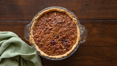 Pecan pie in a glass pie dish on a wooden table with a green waffle towel