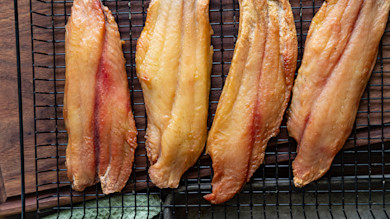 Four smoked catfish fillets on cooling rack over wooden board