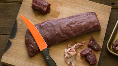 Venison backstrap on cutting board with orange boning knife and trimmed meat pieces