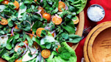 Mixed greens with cherry tomatoes, radish and red onion in wooden bowl; salt and empty serving bowl
