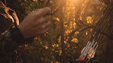 Hunter adjusting compound bow; white-fletched arrows in quiver at sunset