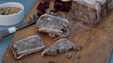 Sliced venison terrine wrapped in bacon on wooden board with mustard and dried cranberries