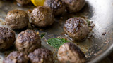 Browned venison meatballs in skillet with mint leaf and lemon wedge
