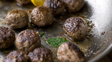 Browned venison meatballs in skillet with mint leaf and lemon wedge