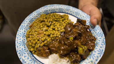 Paper plate of peas and glazed duck over rice held in a hand