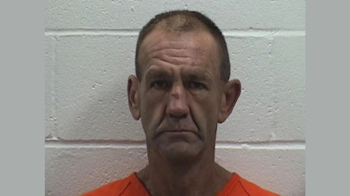 Mugshot of middle-aged man in orange jail shirt standing against cinderblock wall
