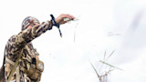 Hunter in camouflage jacket and beanie reaching out, releasing blades of grass