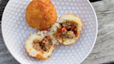 Two golden fried papas rellenas on patterned plate, one split to show seasoned meat filling