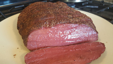 Sliced elk pastrami with pink interior and pepper-crusted exterior on plate